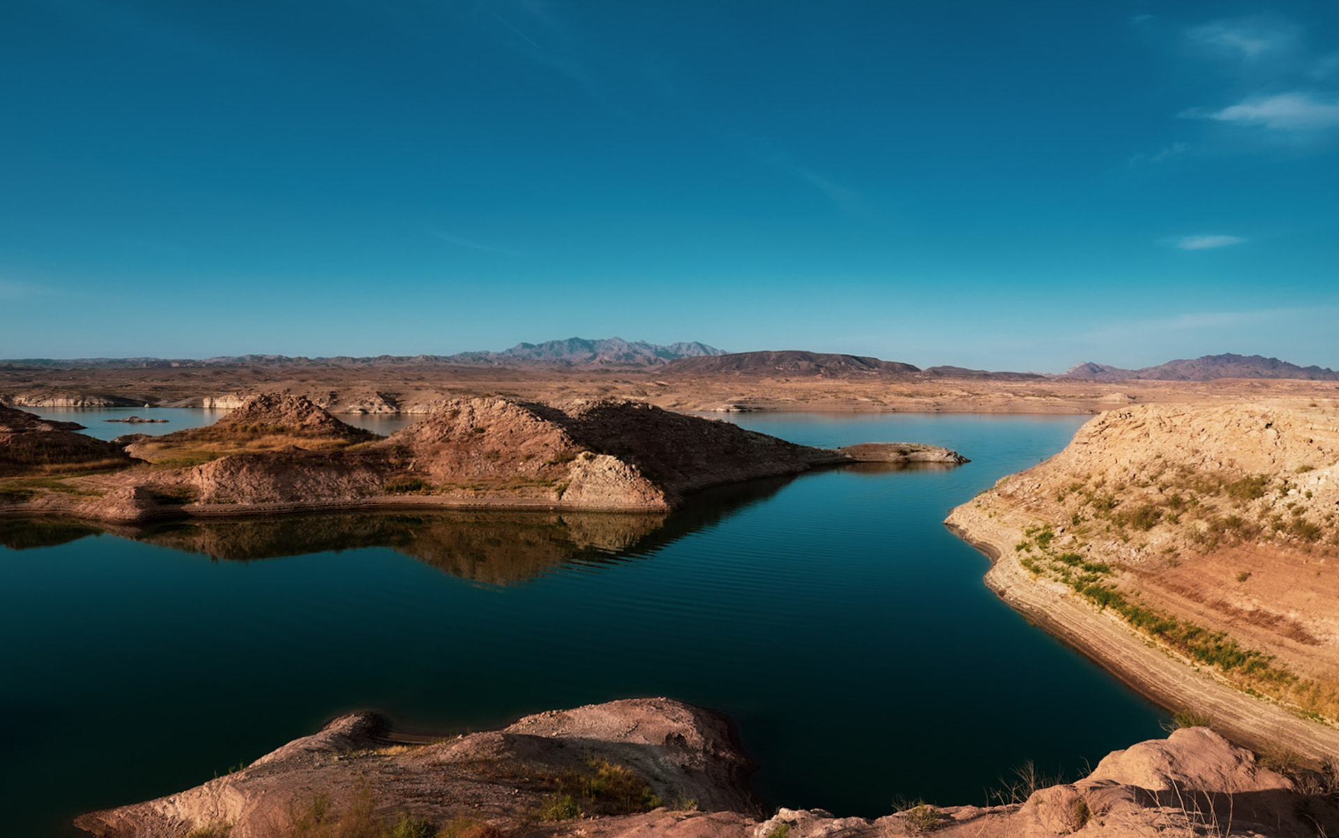 Deep blue lake water winding between red rock desert ridges under a clear sky at Lake Mohave