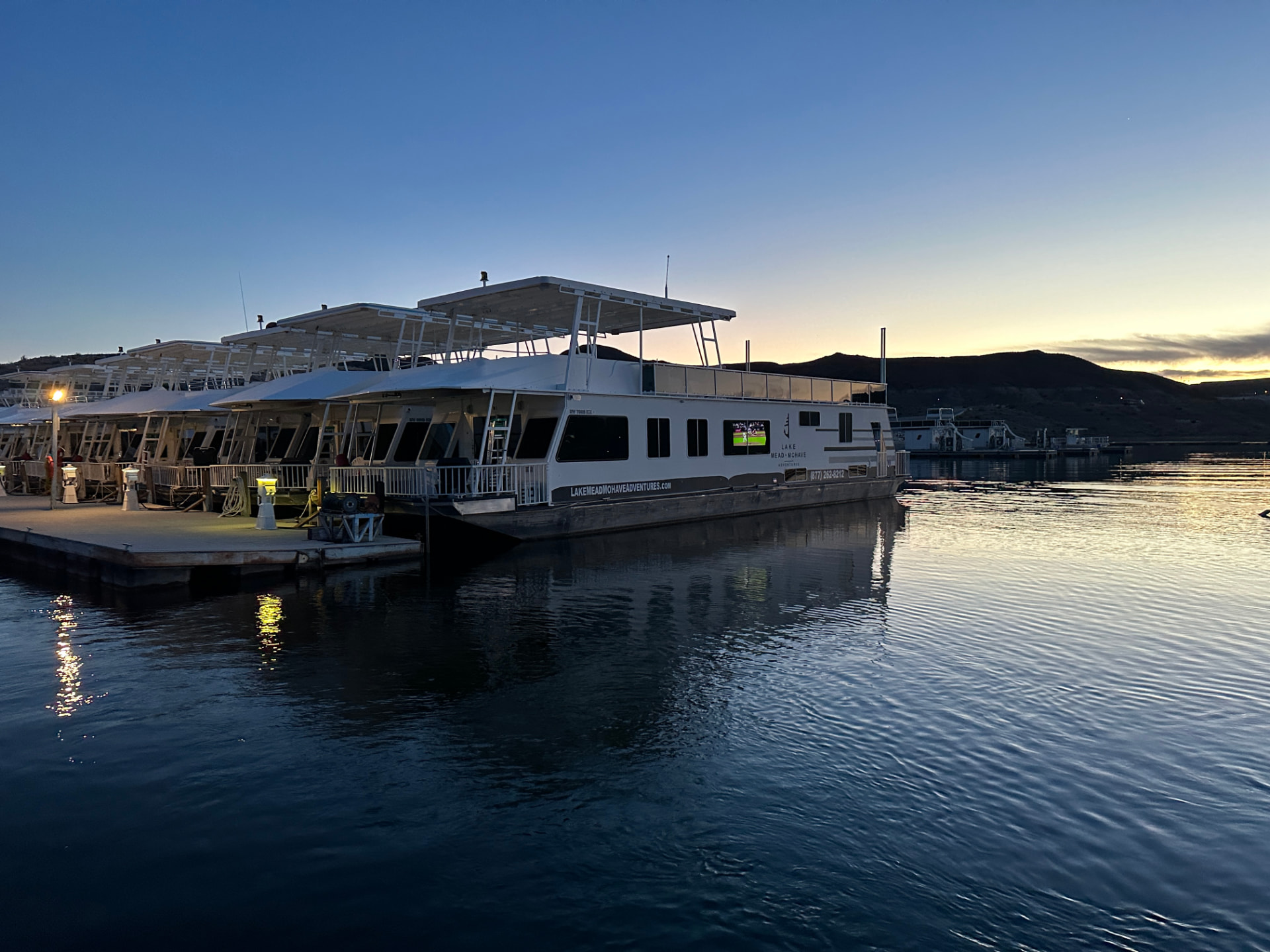 Lake Mead Mohave Adventures houseboat docked at Callville Bay marina at sunset with calm water and desert hills